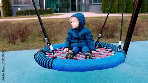 Child enjoys swinging on a large circular swing in a park on a chilly day