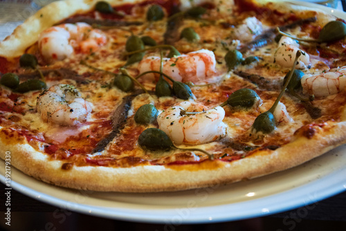 Foodie pizza happiness.  Delicious seafood pizza with shrimps, anchois, capers and mozzarella buffalo served on plate. Traditional Italian cuisine. Simple gourmet lifestyle.	