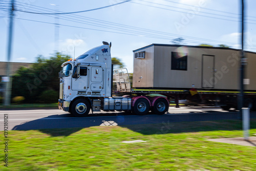 Wallpaper Mural Panning shot of truck transporting worksite building along highway through town Torontodigital.ca