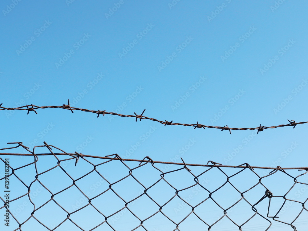 A weathered wire mesh fence with barbed wire secures an unused pasture, creating a clear boundary on the wasteland. A weathered wire mesh fence with barbed wire secures an unused pasture, creating a clear boundary on the wasteland.