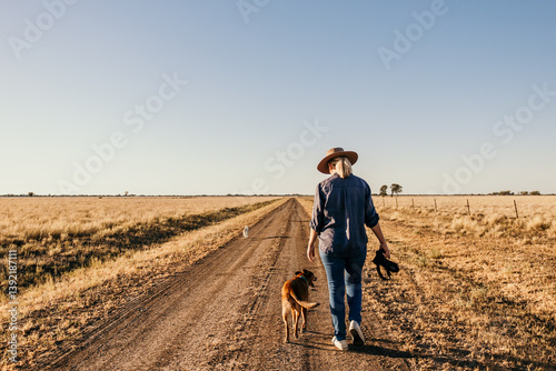 Woman photographer holding camera walking away along road with dog