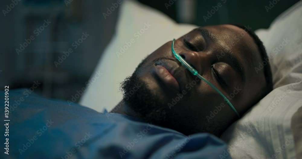 Young African patient lies in a hospital bed with an oxygen tube in his nose, resting quietly.
