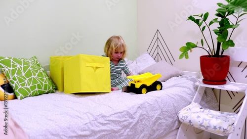 Toddler plays with construction truck in cozy bedroom surrounded by soft toys and colorful decor
