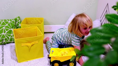 Young child plays with yellow dump truck in cozy playroom surrounded by colorful storage bins