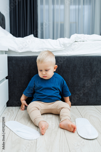 Obraz na płótnie Cute blond toddler boy in blue t-shirt running in spacious hotel room. Toddler boy in comfortable hotel room resting after travel. Child at home sitting on floor w salonie