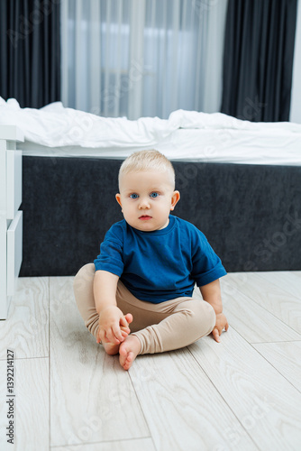 Obraz na płótnie Cute blond toddler boy in blue t-shirt running in spacious hotel room. Toddler boy in comfortable hotel room resting after travel. Child at home sitting on floor w salonie