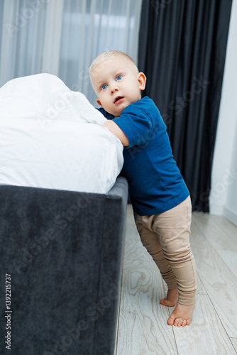 Obraz na płótnie Cute blond toddler boy in blue t-shirt running in spacious hotel room. Toddler boy in comfortable hotel room resting after travel. Child at home sitting on floor w salonie