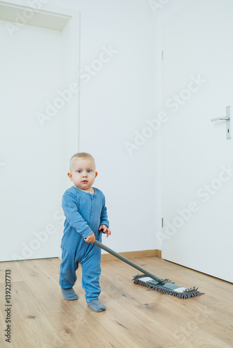 Obraz na płótnie Little boy helper cleaning at home. Blond toddler boy washes the floor with a mop, helping his mother clean at home, free space. Child learns to clean the house. w salonie