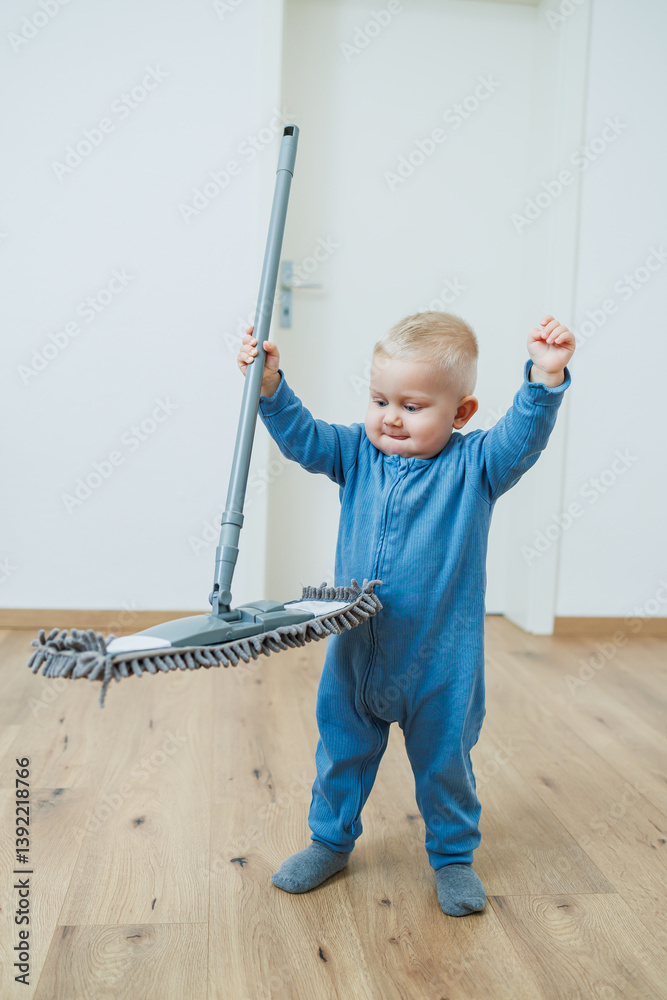 Blond toddler boy washes the floor with a mop, helping his mother clean at home, free space. Child learns to clean the house.