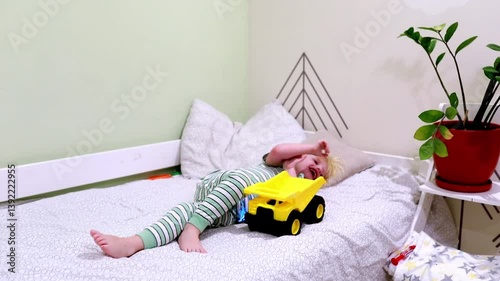 Child playing with toy truck while relaxing on bed in cozy indoor space