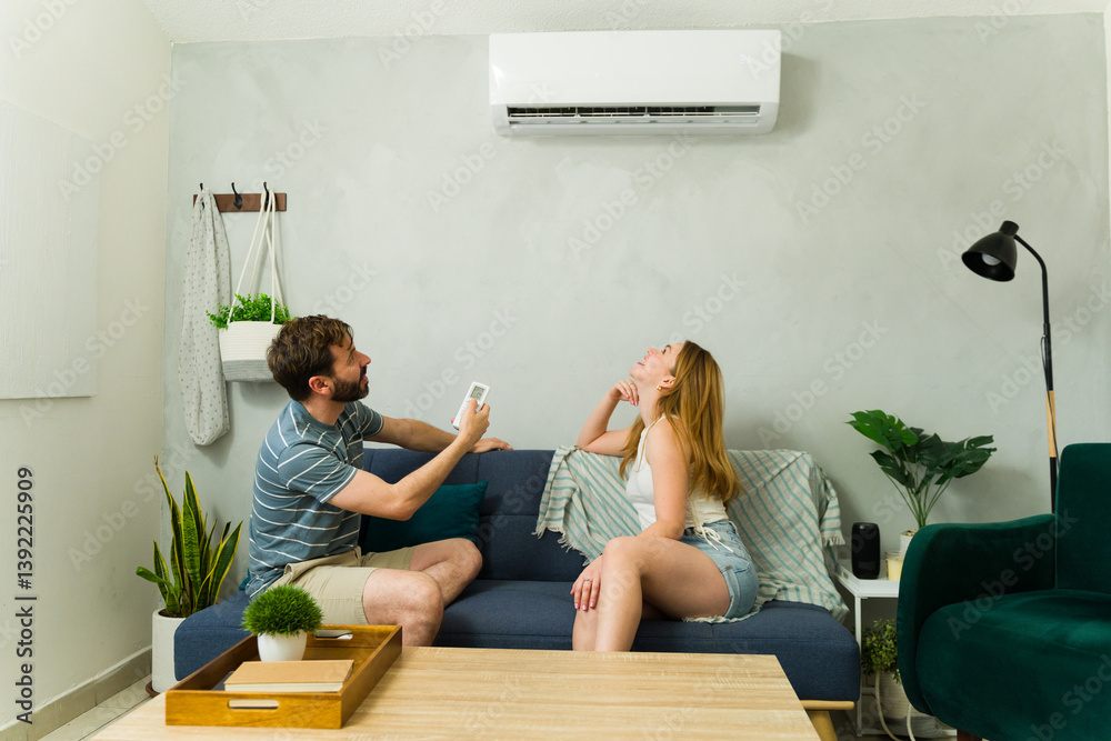 Couple relaxing on sofa using air conditioner remote control during summer heat