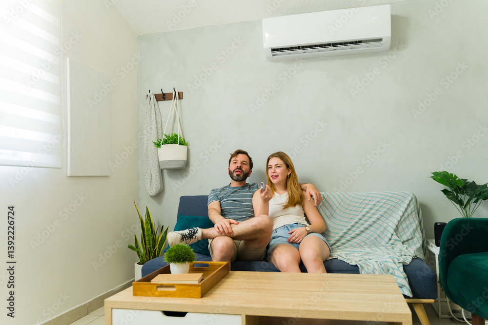 Obraz premium Attractive couple relaxing on sofa with air conditioning unit in living room while watching TV