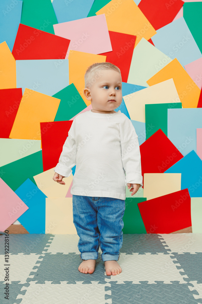 Blue-eyed toddler boy in a white t-shirt and jeans on a bright wall background. Child in stylish casual clothes.