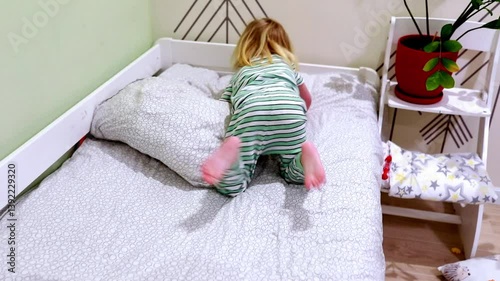 Child plays on bed in cozy room with green decor and a plant while adjusting pillows in playful activity
