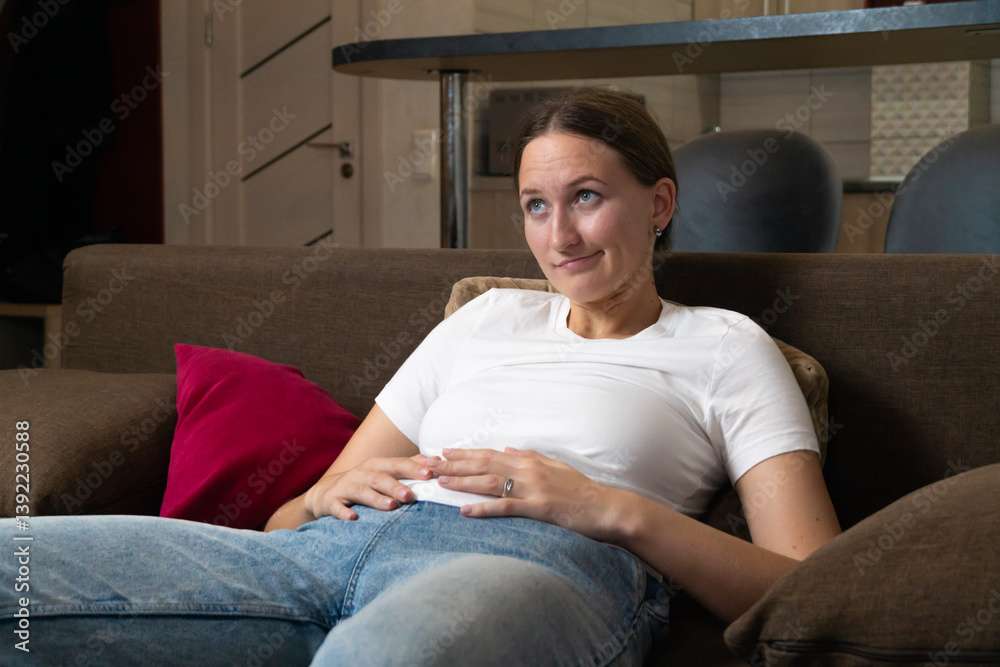 Young woman making a funny face while relaxing on a comfortable sofa in her living room, expressing a playful and carefree attitude