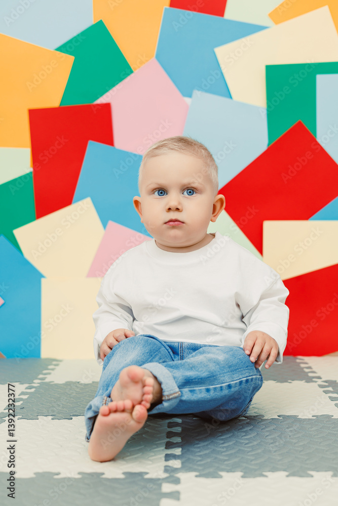 Blue-eyed toddler boy in a white t-shirt and jeans on a bright wall background. Child in stylish casual clothes.