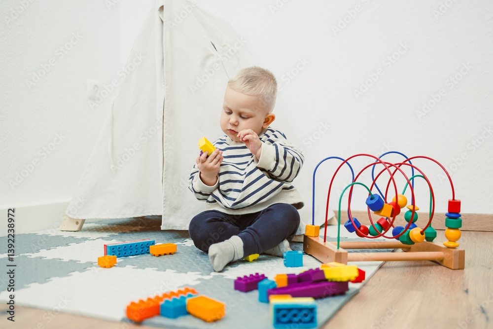 Adorable toddler boy sitting in the living room and playing with educational toys for children. Wooden sorter for child development. Child self-employment. Development of thinking in toddlers.