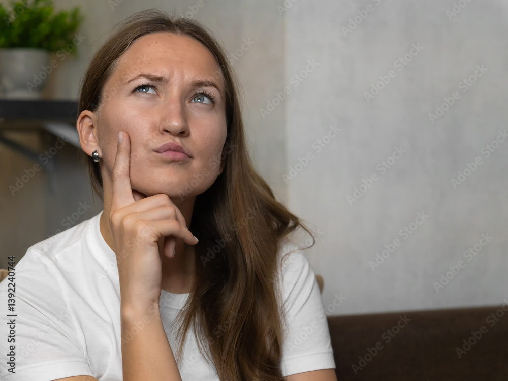 Young woman sits on a couch, her hand on her chin, deep in thought as she contemplates a decision in the comfort of her home
