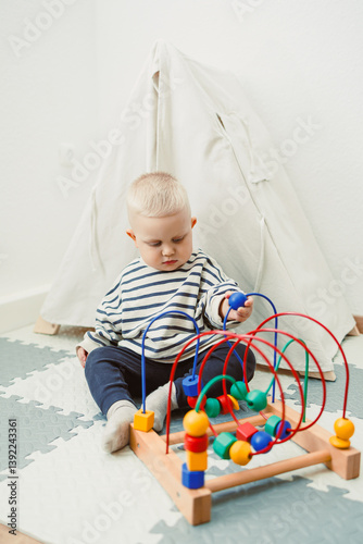Adorable toddler boy sitting in the living room and playing with educational toys for children. Wooden sorter for child development. Child self-employment. Development of thinking in toddlers.