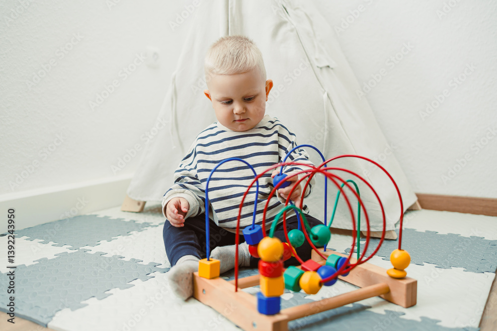 Adorable toddler boy sitting in the living room and playing with educational toys for children. Wooden sorter for child development. Child self-employment. Development of thinking in toddlers.