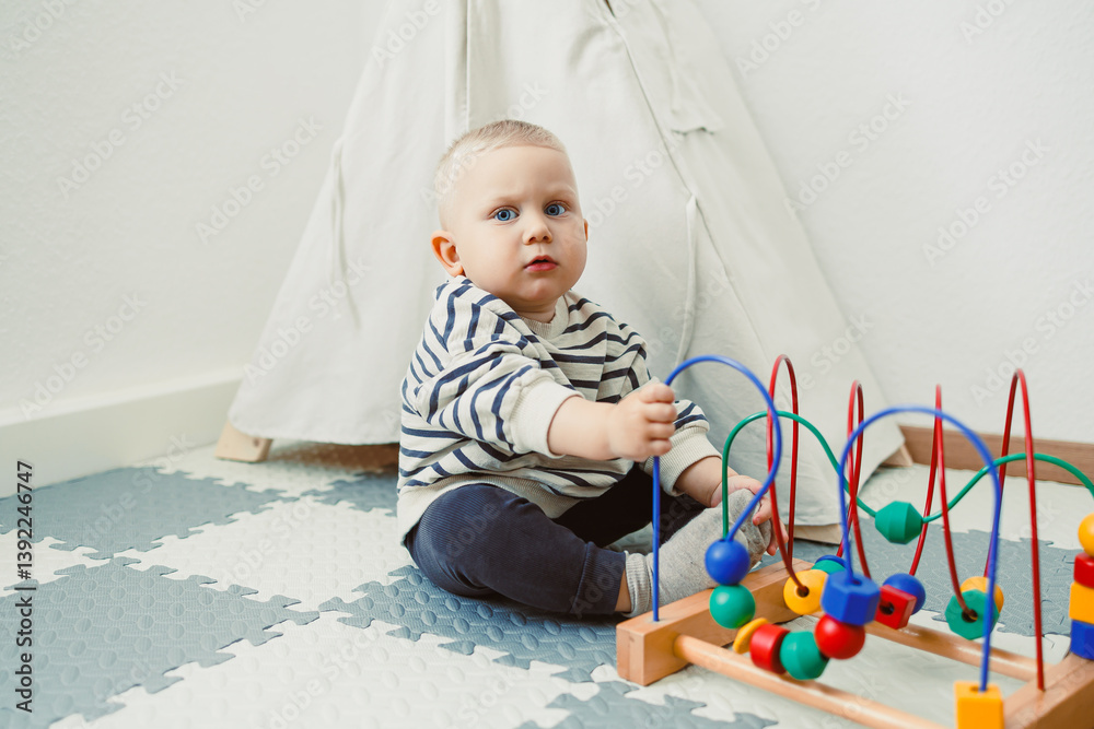 Adorable toddler boy sitting in the living room and playing with educational toys for children. Wooden sorter for child development. Child self-employment. Development of thinking in toddlers.