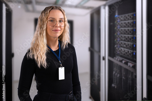 Female IT professional in datacenter with confident expression wearing security identification badge. IT consultant in server and network room