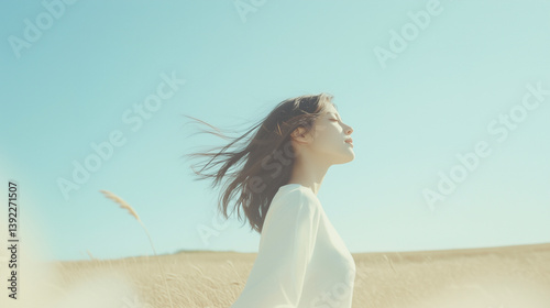 青空の下、風に髪をなびかせて目を閉じる女性のポートレート（自然・癒し・美容・広告） photo