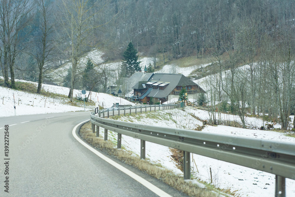 Obraz premium Winding road leads through tranquil snowy landscape towards a cozy cabin nestled in the mountains during a quiet winter day