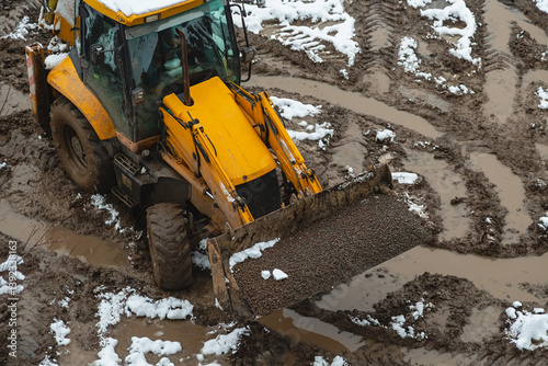Photography A loader tractor with a bucket filled with gravel is driving through muddy and wet off-road at a construction site