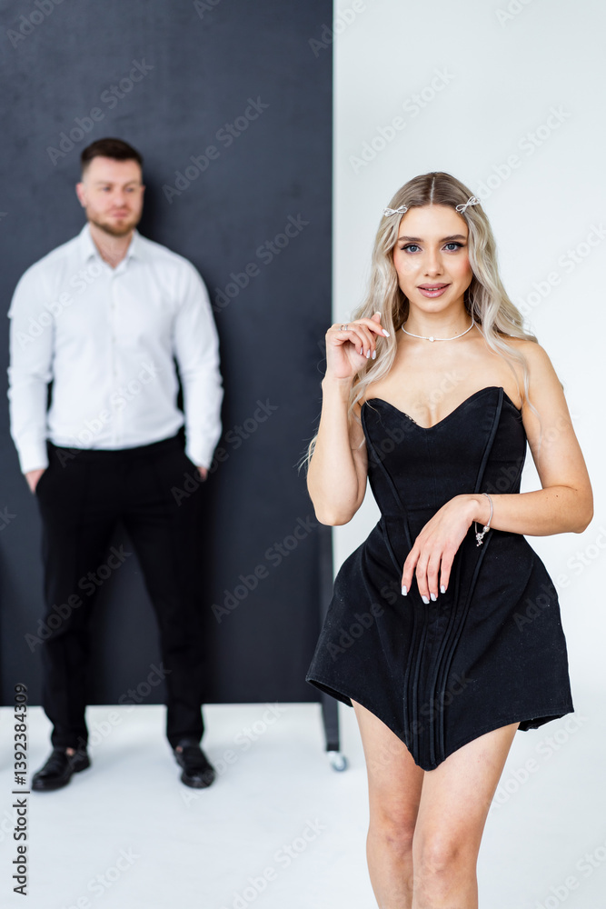 Obraz premium Couple in modern studio. A woman in a stylish black dress stands confidently in front of a man wearing a white shirt and black pants.