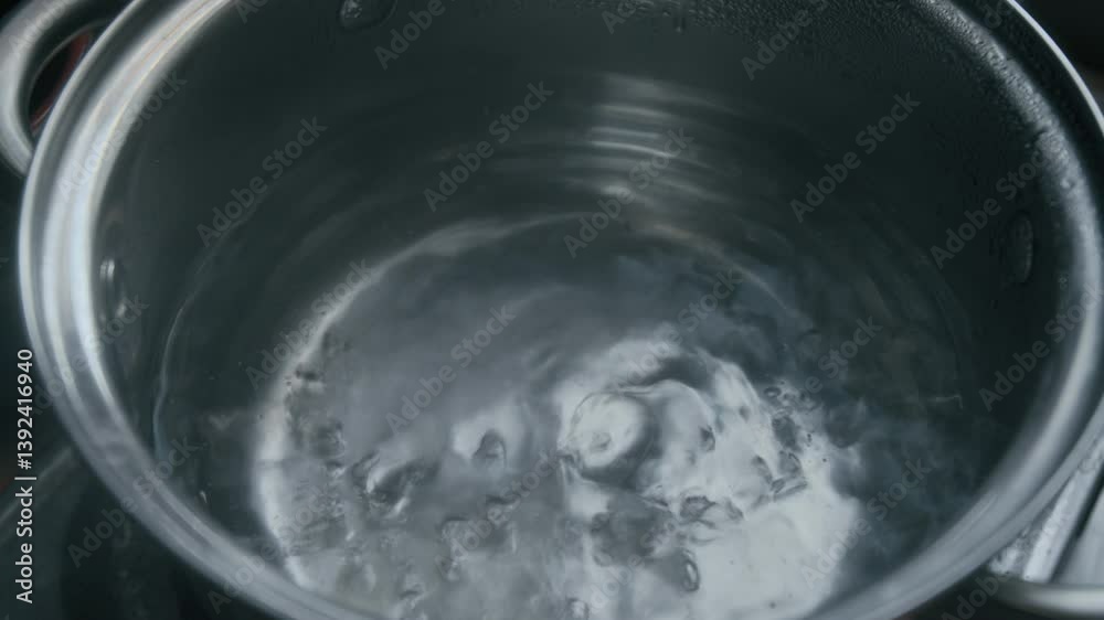 Close-up high angle shot of boiling water swirling in shiny stainless steel pot on portable stove Close-up high angle shot of boiling water swirling in shiny stainless steel pot on portable stove