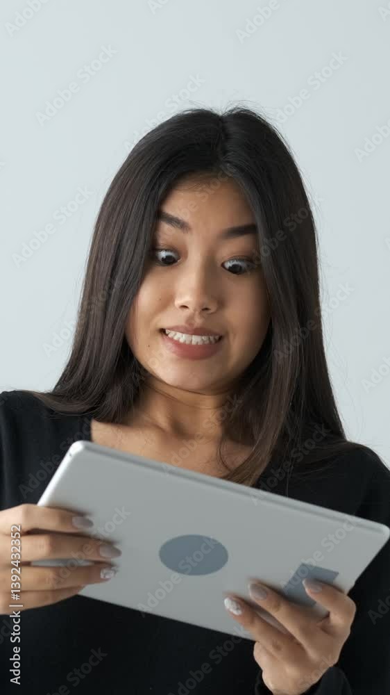 Focused Asian woman playing a video game on a tablet PC, fully engaged in the digital activity on a white background, emphasizing leisure and concentration. Vertical video. Focused Asian woman playing a video game on a tablet PC, fully engaged in the digital activity on a white background, emphasizing leisure and concentration. Vertical video.