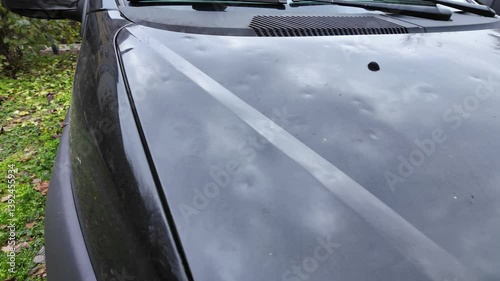 Hood of a black car damaged by hail storm. Dents caused by ice grains. Parking outdoors in extreme weather conditions. Everyday problems, car insurance concept.
