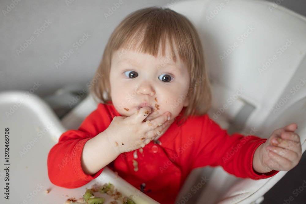 Naklejka premium A small child eats buckwheat porridge on his own.