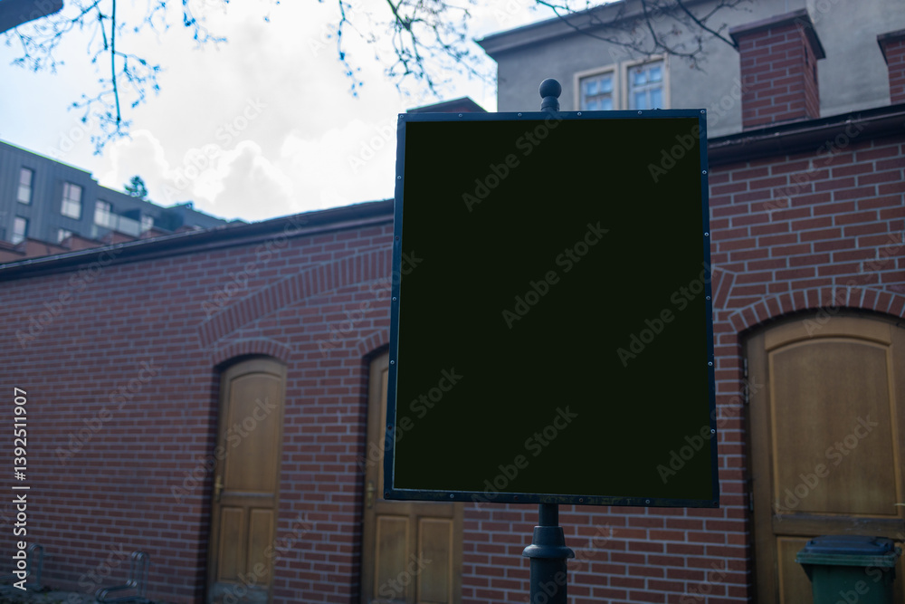 Blank signpost on a street corner stands next to a brick wall with wooden doors. The empty signboard can be used for various purposes, like inserting custom messages or advertisements