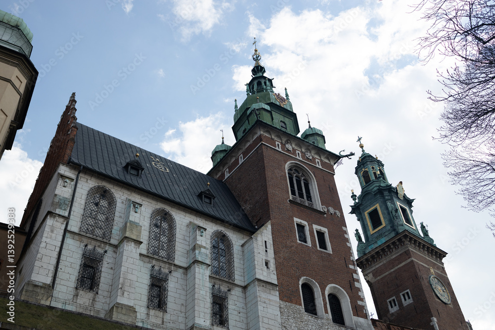 Historic cathedral building in Krakow, Poland, featuring tall towers and intricate architecture. The photo is taken against a clear blue sky, highlighting the grandeur and beauty of the church