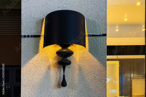 Black metal wall lampshade with warm light on concrete surface. Yellow illumination in dark shade. Exterior decor of modern hotel, evening time, outdoor lights on, elegant shape lighting closeup.