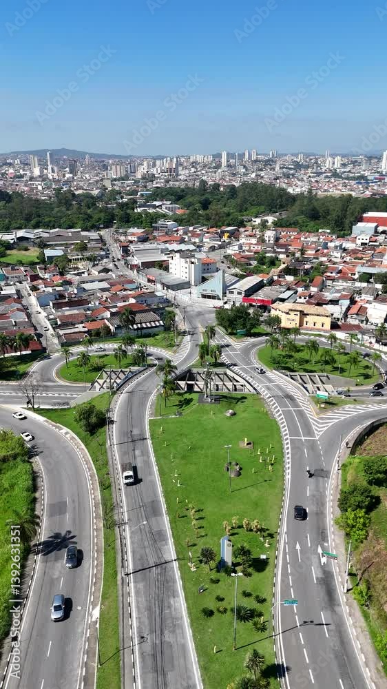 Visão aérea vertical da entrada da cidade de Mogi das Cruzes, em São Paulo, destacando o monumento à Bandeira, vias de acesso e paisagem urbana ao redor da estrutura simbólica
