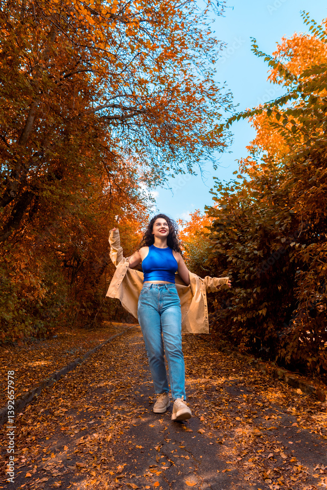Fototapeta premium Millennial woman walking on an alley covered with autumn leaves