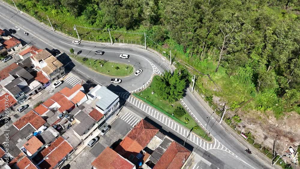 Visão aérea de uma rotatória de trânsito em um dia ensolarado, com carros em movimento fluindo pelas ruas, capturada por drone, destacando a dinâmica do tráfego urbano e a infraestrutura rodoviária