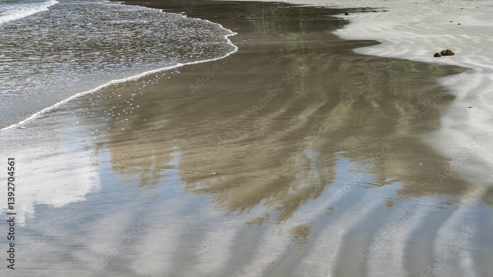 Ocean waves are spreading across the sandy beach. Delicate foam, wavy pattern and reflection on wet smooth sand. Close-up. Ocean waves are spreading across the sandy beach. Delicate foam, wavy pattern and reflection on wet smooth sand. Close-up.