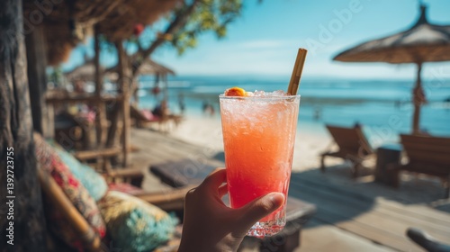 A person is holding a glass of pink drink on a beach