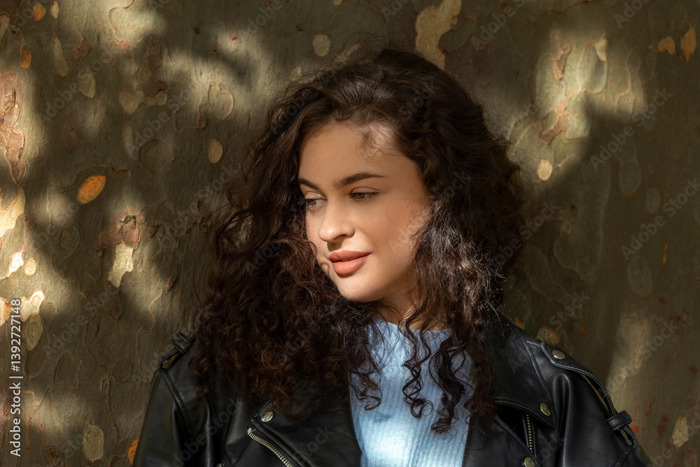 Curly hair woman portrait in nature, against a tree trunk Curly hair woman portrait in nature, against a tree trunk