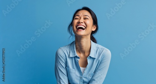Indonesian 20s woman on blue plain bright background happy laughing hysterical looking at camera portrait banner with copy space ad concept marketing