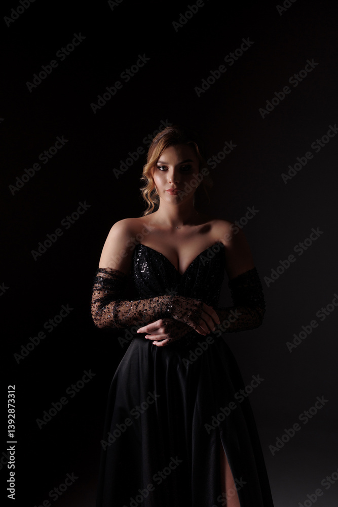 Elegant woman in black evening gown with lace gloves poses in dramatic lighting Elegant woman in black evening gown with lace gloves poses in dramatic lighting