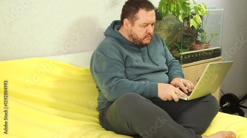 Funny fat man with laptop on bed.