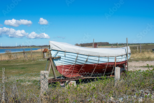 Fototapeta Naklejka Na Ścianę i Meble -  Old fishing boat on the beach. The boat is on the seashore on the sand. The Baltic Sea in spring on a sunny day. Nature. Blue sky and clouds.