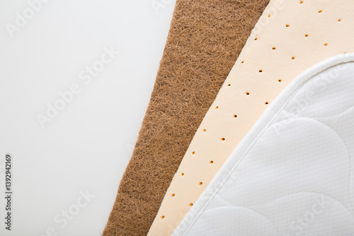 Brown coconut coir, yellow rubber foam and white cloth cover of orthopedic mattress on light gray table background. Different inside layers. Closeup. Top down view.