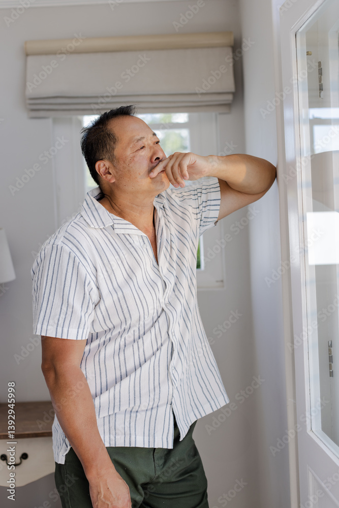 Senior man thoughtfully looking out window at home, wearing striped shirt Senior man thoughtfully looking out window at home, wearing striped shirt