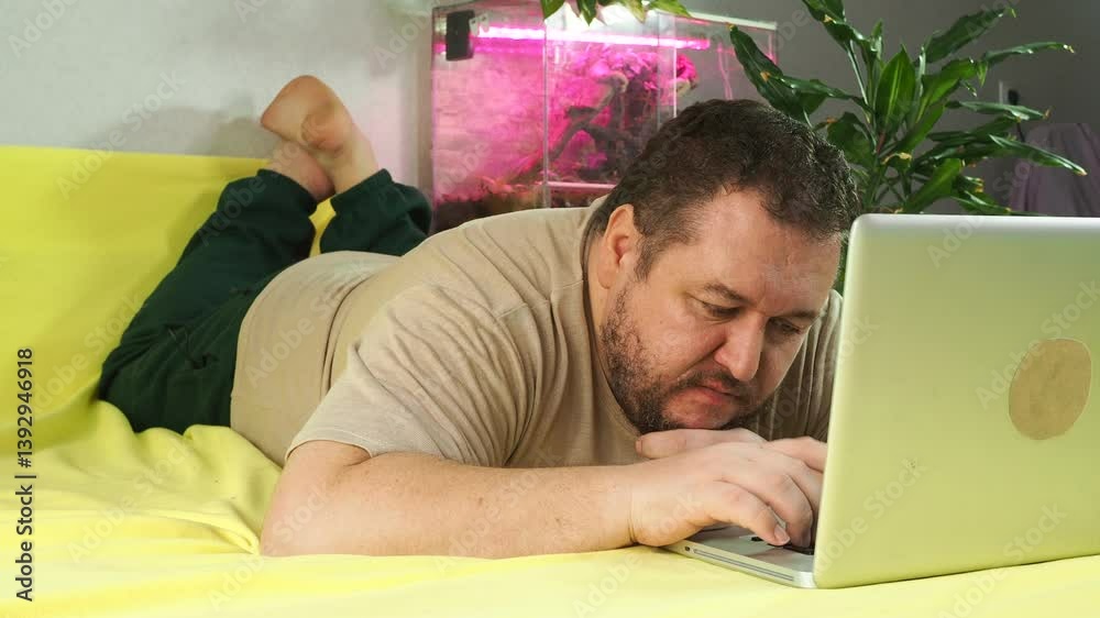 Funny fat man with laptop on bed.